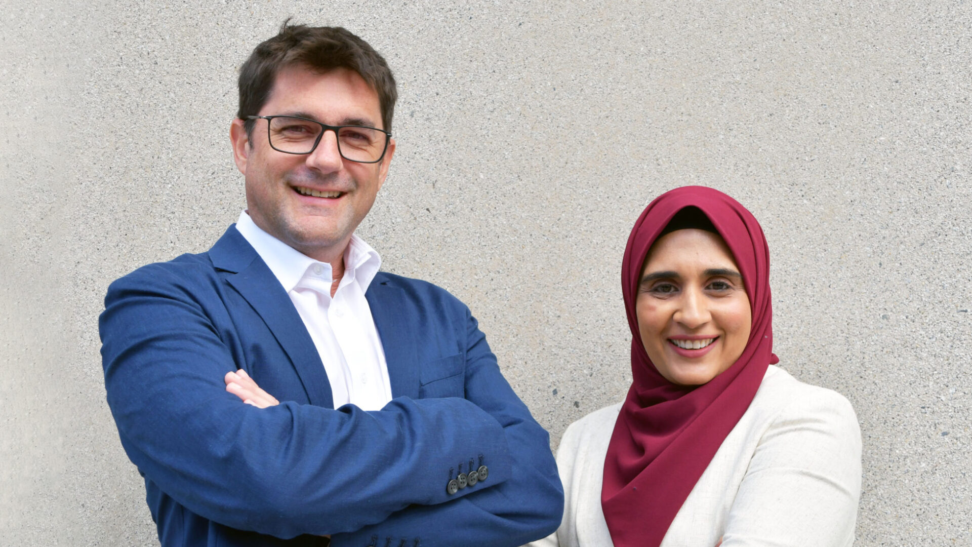 Image shows Allotype co-funders Jim Robinson (standing left) and Lubna Shafi (standing right). Both are smiling to camera.